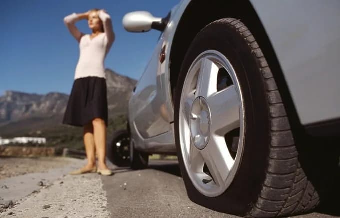 Automobilist langs de weg naast een auto met een lekke voorband